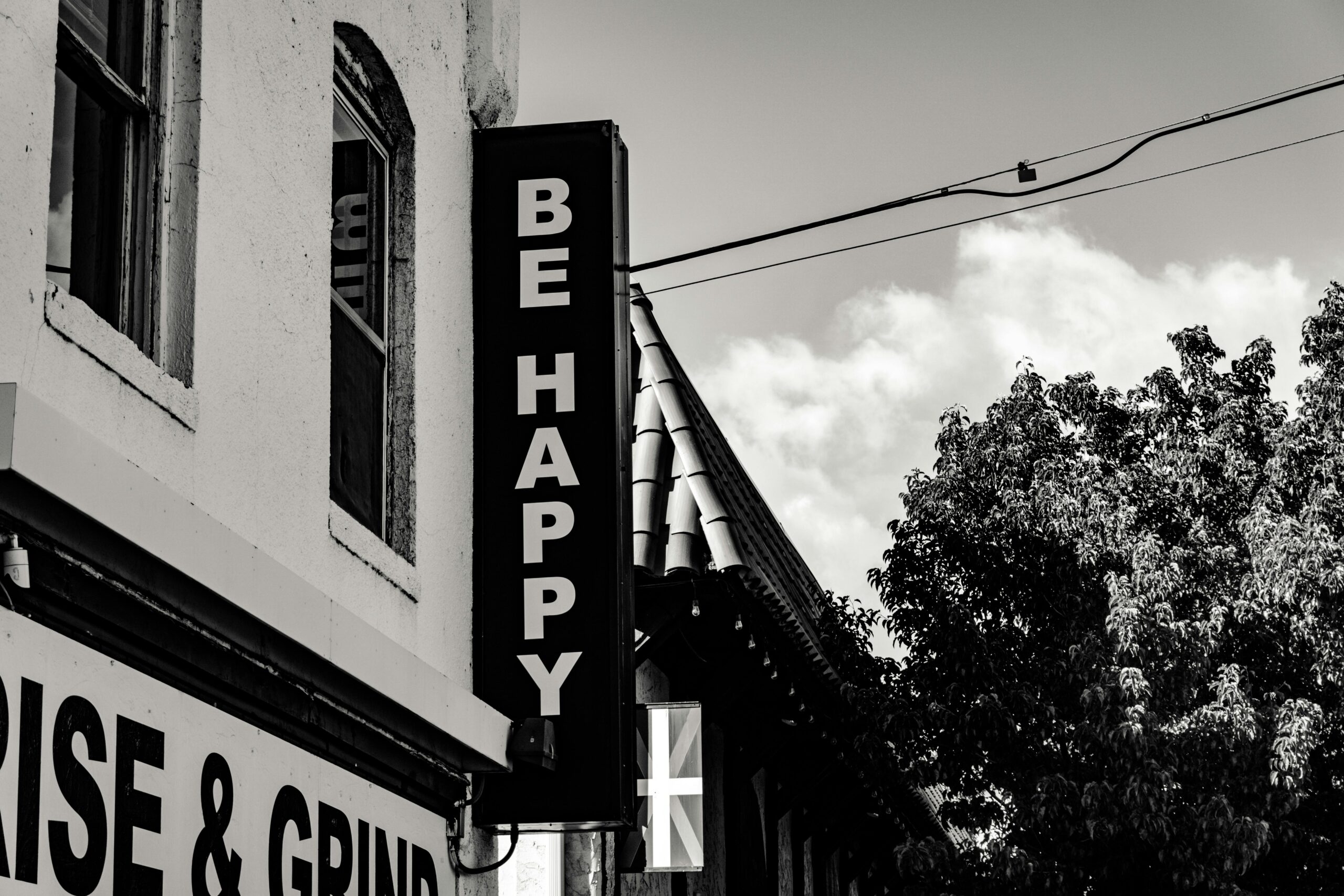 Monochrome image of exterior signage reading Be Happy on a building corner.