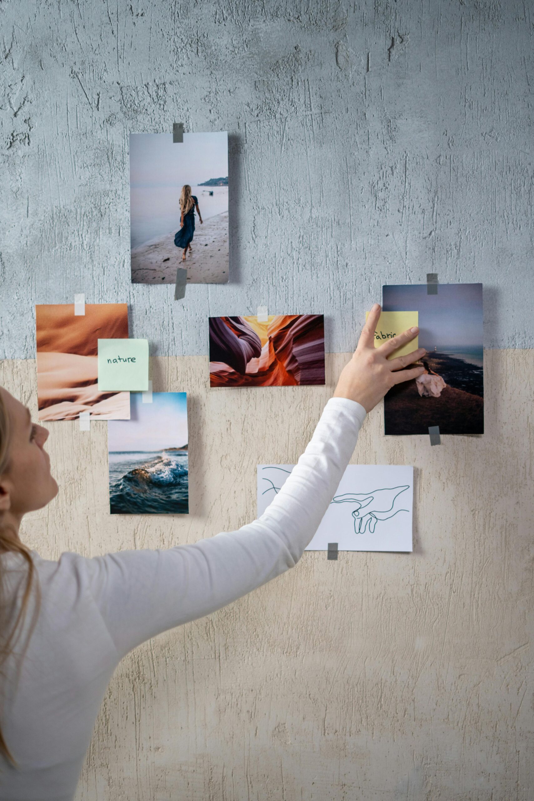 Achieve Your Goals Faster and Easier with an Effective Vision Board or Dream Box A woman arranging photos and sticky notes on a textured wall, enhancing a creative moodboard.